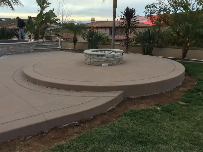Tiered circular concrete patio with a stone fire pit on a lawn