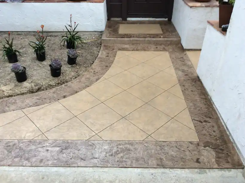 Diamond-pattern stamped concrete entry framed by a dark textured border beside potted succulents