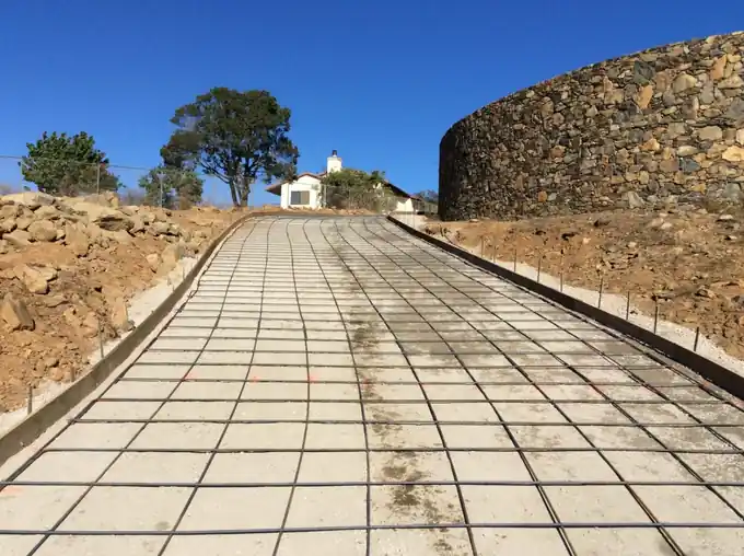 Long formed concrete road with a tied rebar grid running down a hillside before the pour