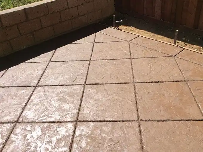 Large stamped tile-pattern concrete patio against a block wall