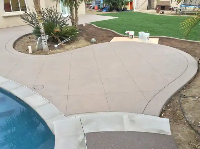 Curving pool edge with a concrete deck and a strip of lawn filled in beside it
