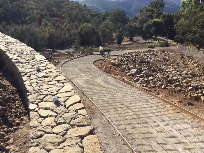 Rebar-gridded stamped walkway in progress beside a stone wall
